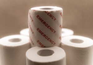 This is a picture of six rolls of toilet paper. Five on the bottom with one on top. There is red writing on the top roll that say emergency over and over